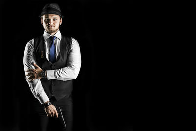 Portrait of businessman holding gun while standing against black background