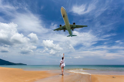 Full length of man standing on airplane at beach against sky