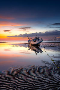 Fishing boat moored on shore at beach during sunset