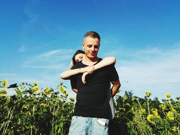 Low angle view of happy couple standing on field against blue sky during sunny day