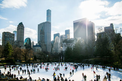 People ice skating by modern buildings against sky