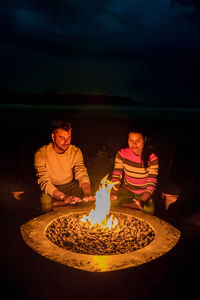 Couple sitting by campfire at night