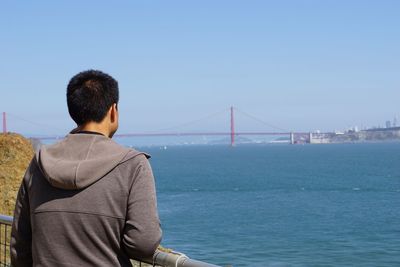 Rear view of man on bridge over sea against clear sky