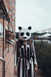 Person wearing mask against building in city against sky