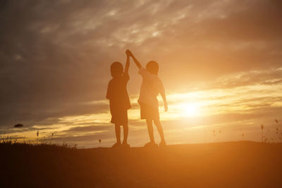 Friends standing on land against sky during sunset