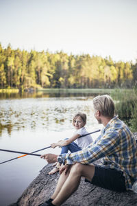 Smiling daughter looking at father while fishing at lake