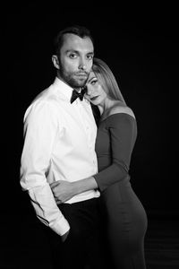 Portrait of elegant couple standing against black background