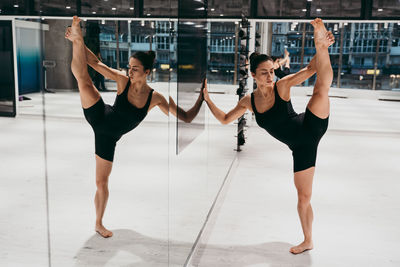 Full length of woman stretching while standing by mirror at gym