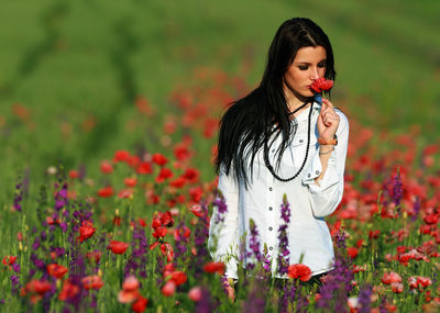 Beautiful young woman standing by poppy flowers in field