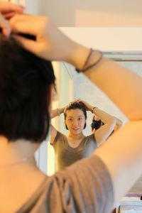 Woman tying hair while looking into mirror