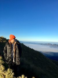 Rear view of man standing on mountain against clear blue sky