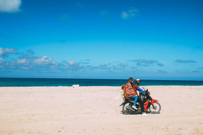 People riding motorcycle at beach against blue sky during sunny day