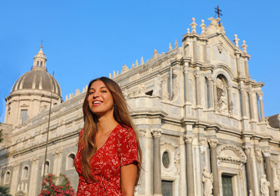 Portrait of smiling woman standing against building and sky