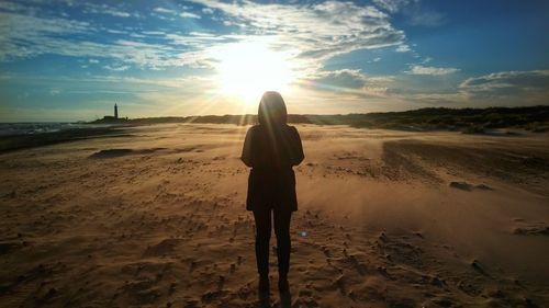 Woman standing on sand at beach against cloudy sky during sunset