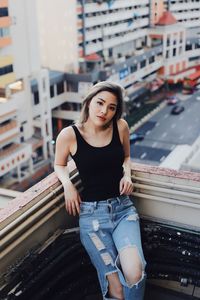 Portrait of young woman wearing torn jeans standing against building in balcony
