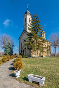 View of church and trees by building against blue sky