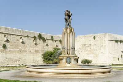 Statue against fountain against clear blue sky