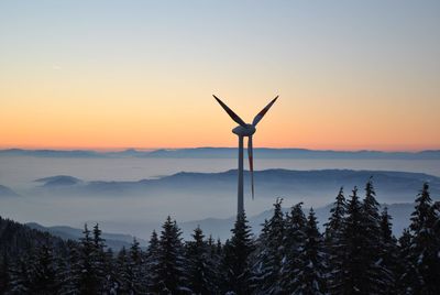 Windmill in forest against sky during sunset