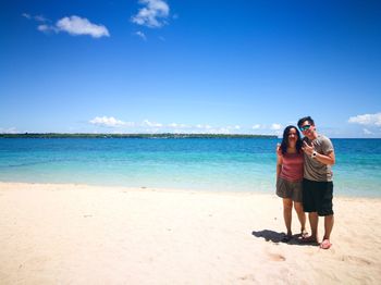 Young couple standing on beach against blue sky