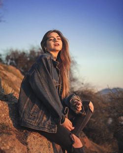 Young woman smiling while sitting on land against sky