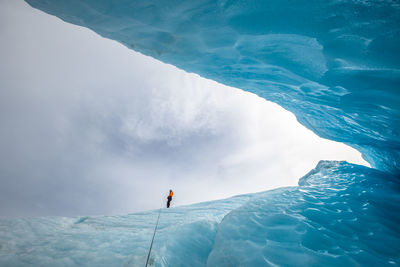 Low angle view of person standing on ice at strupbreen against cloudy sky