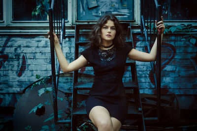 Portrait of young woman sitting on steps against abandoned building