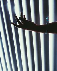 Close-up of human hand wearing bracelet against window blind