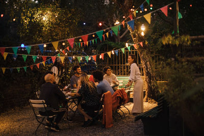 Multi-ethnic male and female friends enjoying dinner party in illuminated backyard