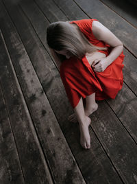 High angle view of sadness woman in red dress sitting on wooden floor