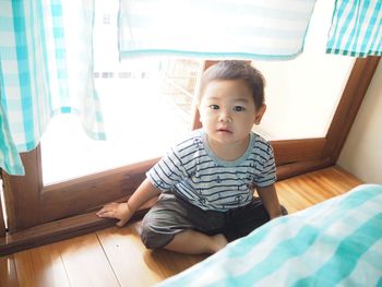 High angle portrait of cute toddler sitting on hardwood floor by door in bedroom