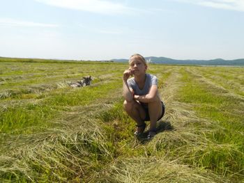 Portrait of girl crouching on grassy land against sky