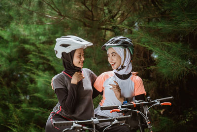 Young smiling friends sitting on bicycle against trees