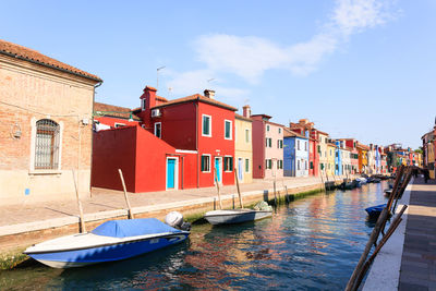 Boats moored in canal by buildings against sky