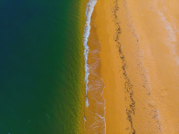 Sandy sunny beach and deep turquoise sea with white waves aerial view