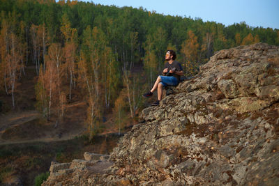 Full length of man sitting on rock in forest