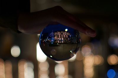 Cropped hand holding crystal ball with reflection of illuminated buildings