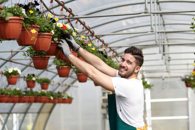 Young man holding potted plant in greenhouse