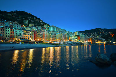 Illuminated buildings by river against sky at night