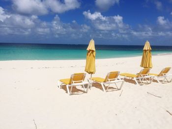 Deck chairs at beach against sky