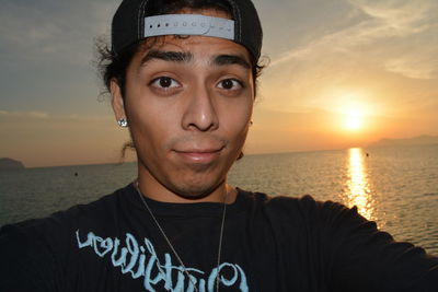 Portrait of young man at beach against sky during sunset