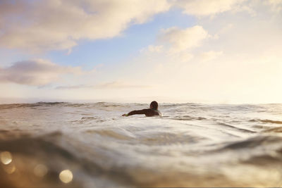 Male surfer swimming at sea against sky