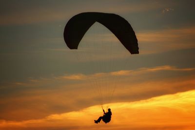 Silhouette person paragliding against sky during sunset