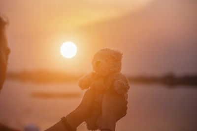 Woman standing by sea against sky during sunset