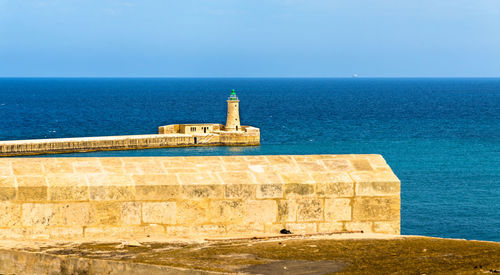 Lighthouse by sea against blue sky