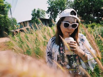 Portrait of young woman drinking juice while standing against plants