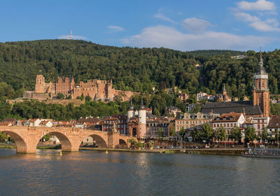 Arch bridge over river by buildings against sky