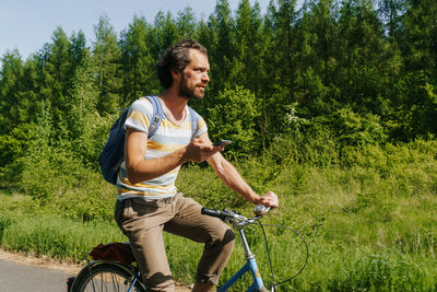 Man using mobile phone while riding bicycle by grassy field