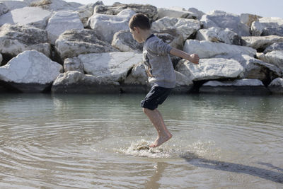 Side view of playful boy jumping on shore at beach in water