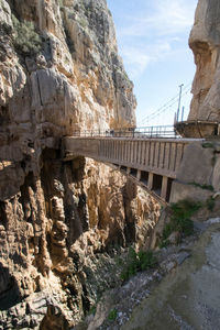 Bridge over river by rocky mountains against sky