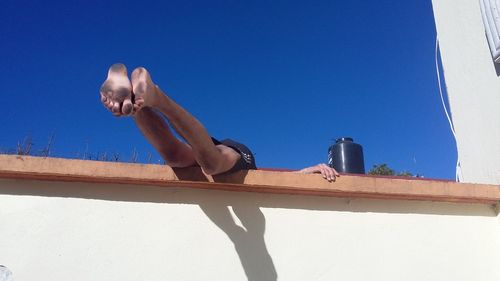 Low angle view of shirtless man against blue sky